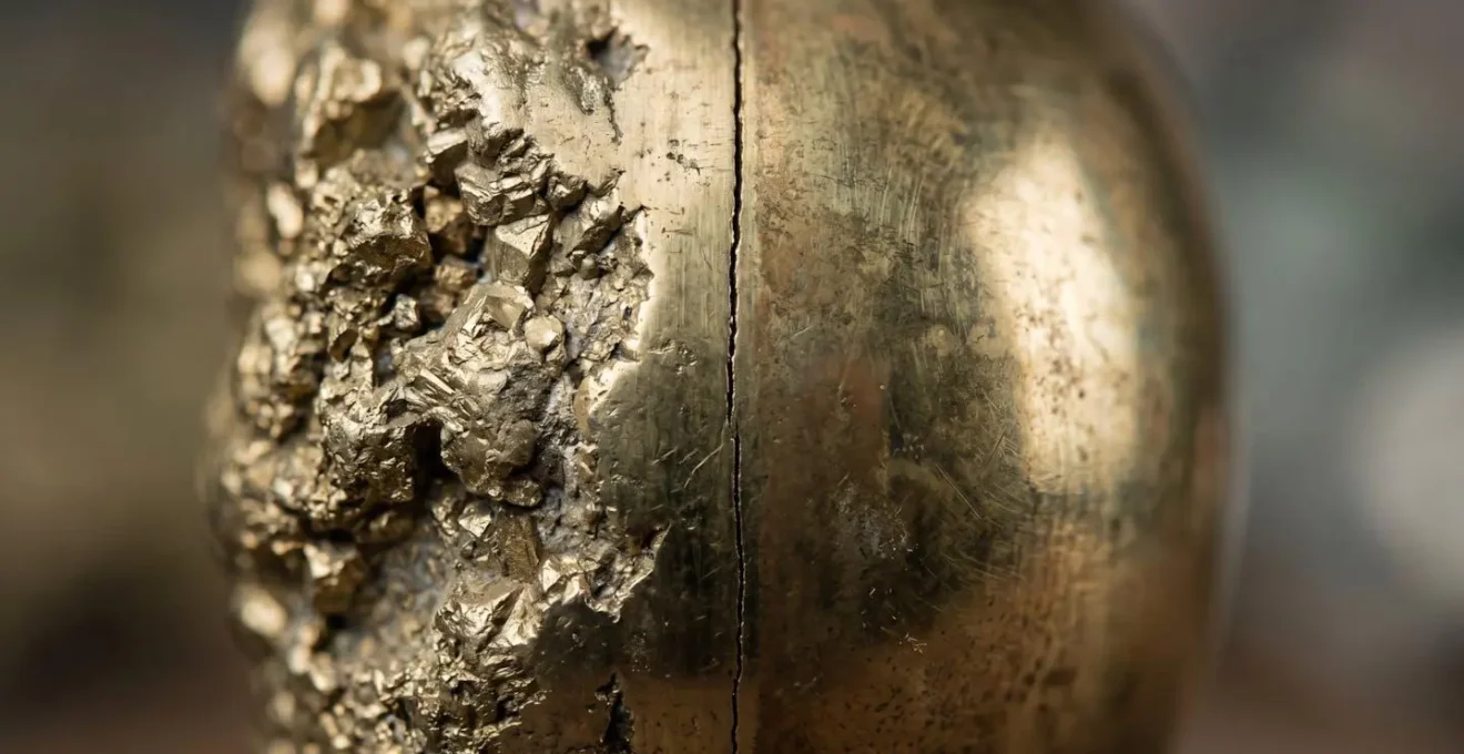 A macro shot showing a crack between a piece of raw gold ore and a piece of tarnished brass, symbolizing a breakdown in correlation between gold and government bonds.