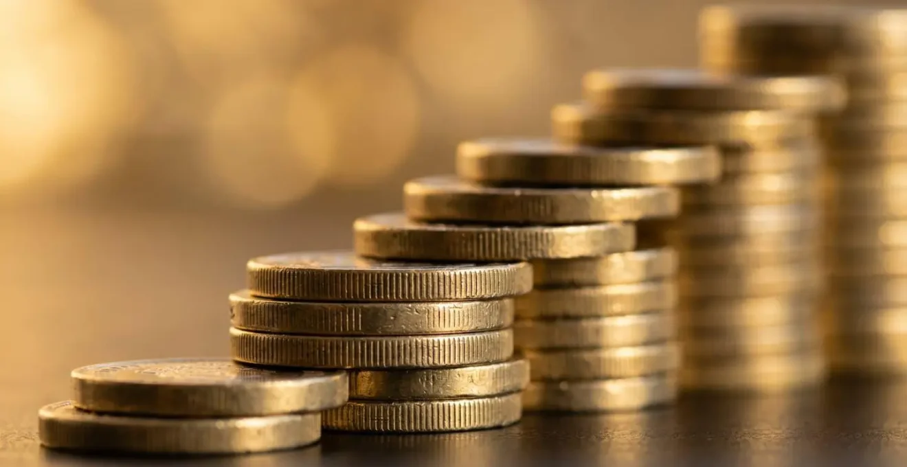 Macro shot of stacked British coins forming ascending steps with soft golden hour lighting
