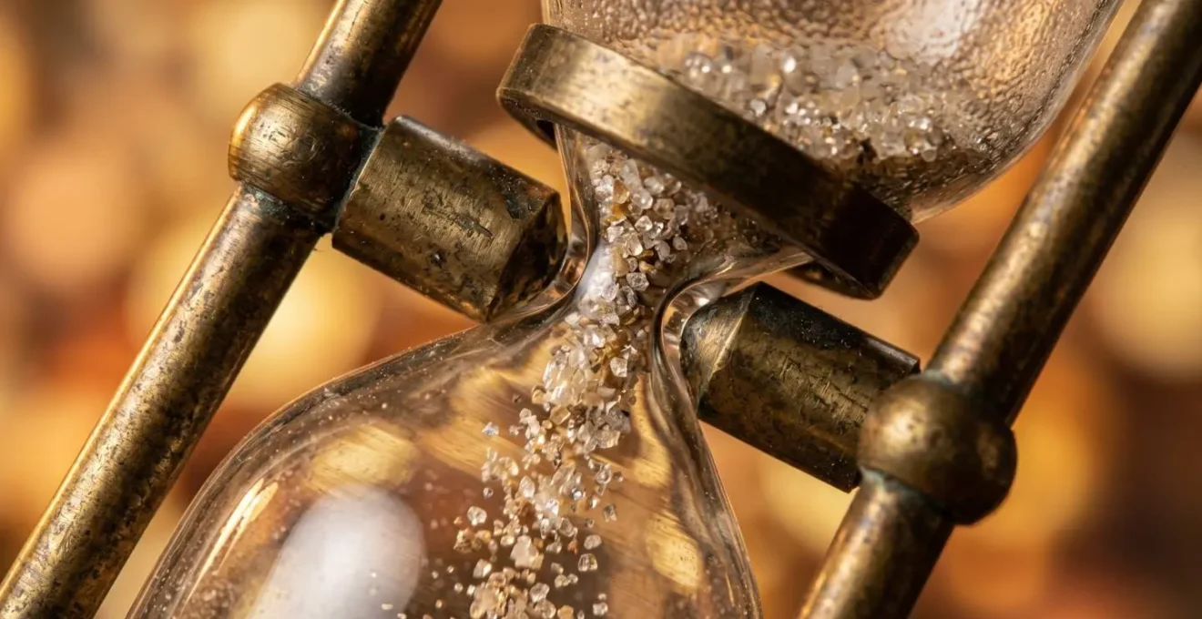 Macro photograph showing sand flowing through an hourglass with reflective particles suggesting lost investment opportunity